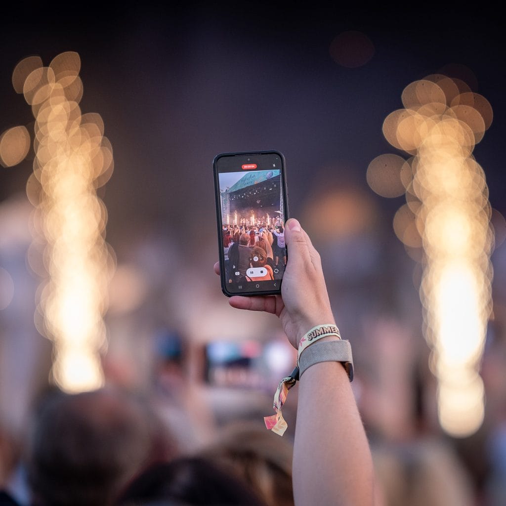 A person taking a picture of fireworks at a concert.