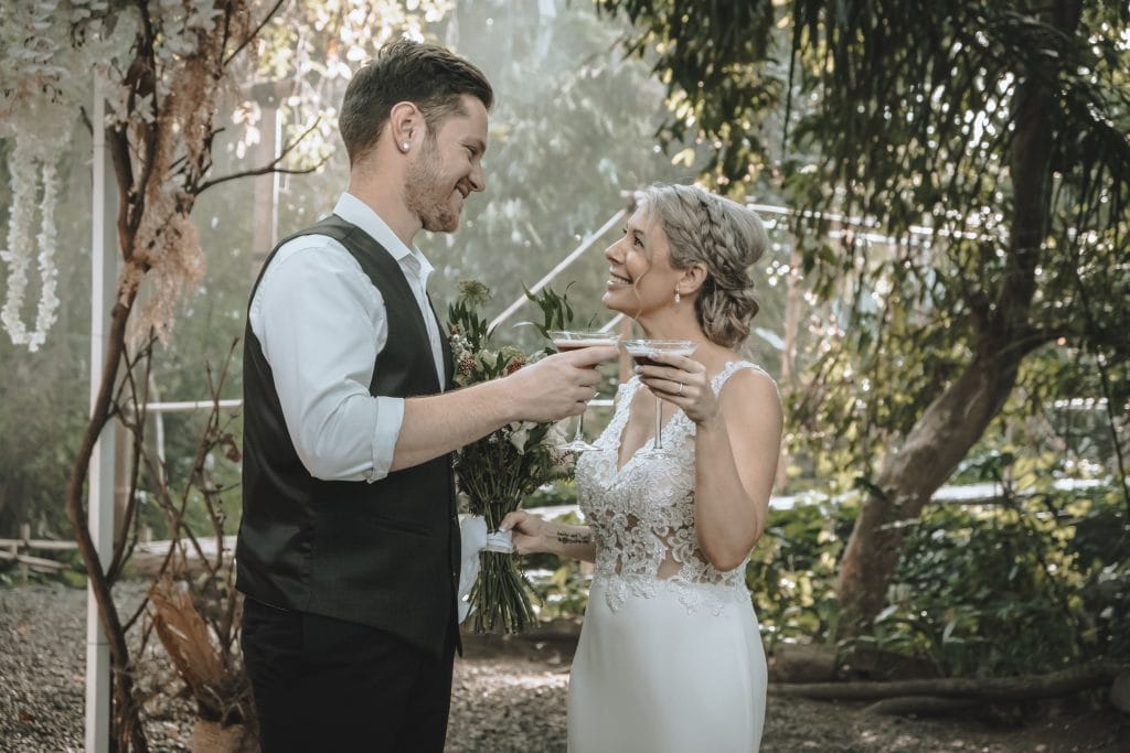 A bride and groom sharing a cup of coffee in the woods.
