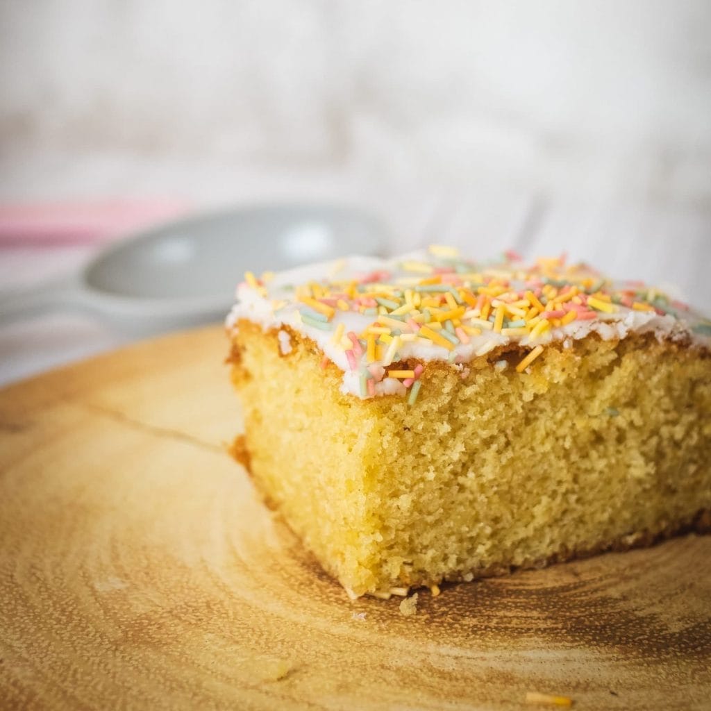 A slice of cake with sprinkles on a wooden plate.