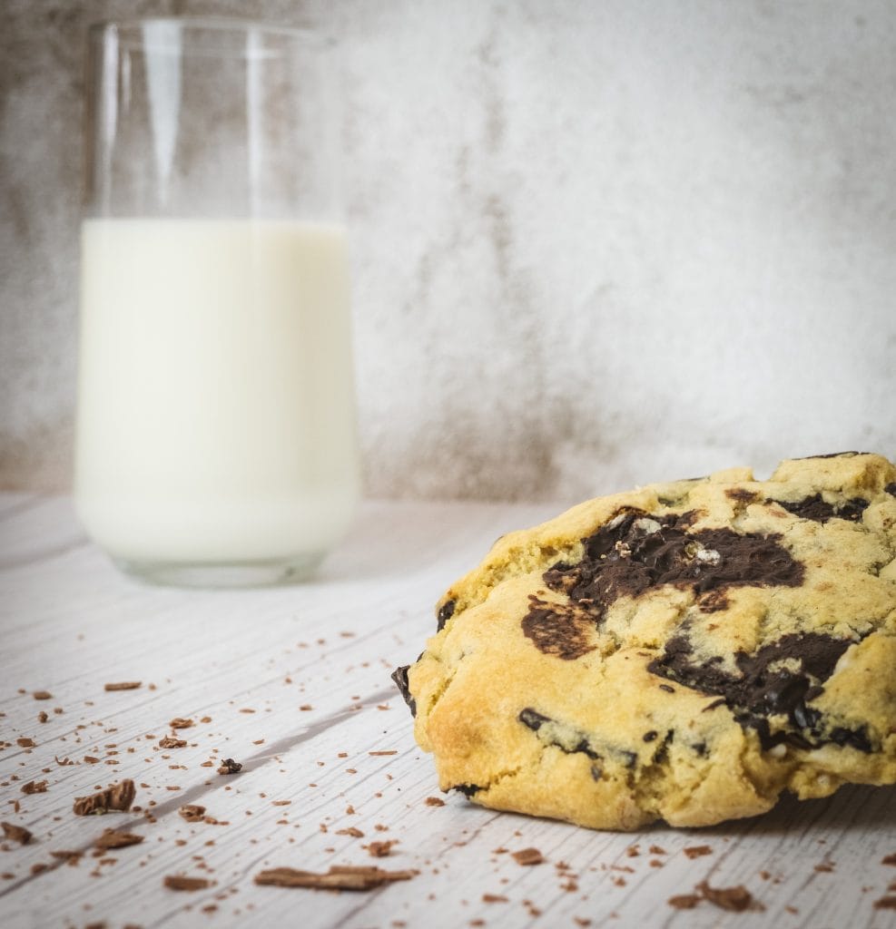A chocolate chip cookie next to a glass of milk.