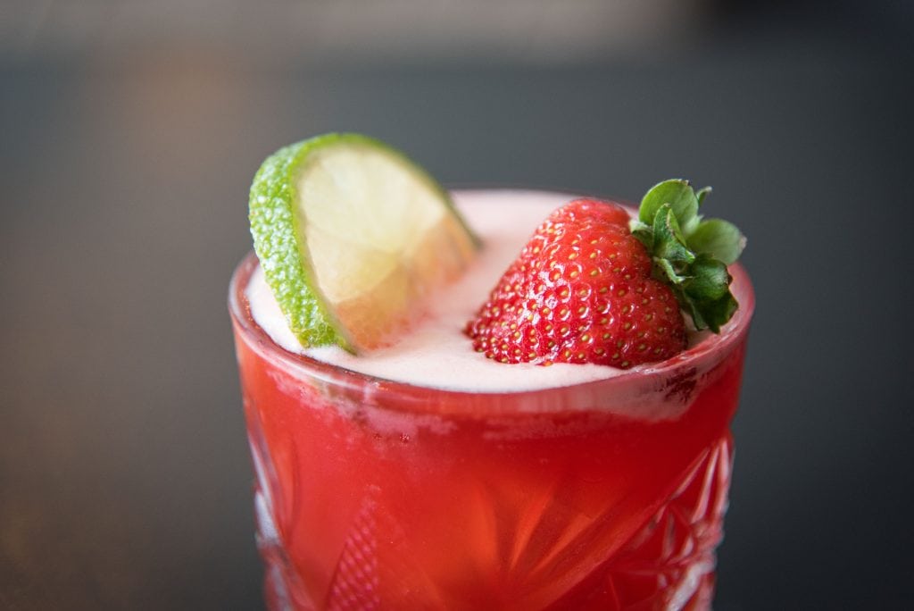 A cocktail with a strawberry and lime garnish.