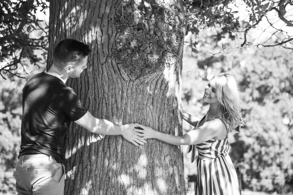 A black and white photo of a couple hugging a tree.