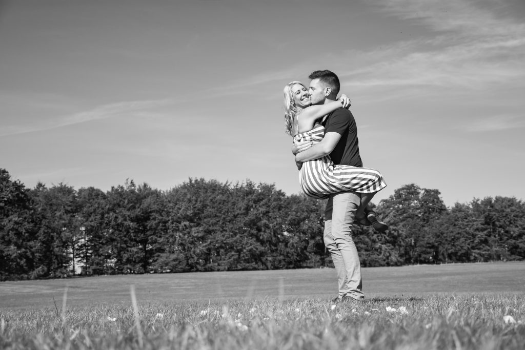 A black and white photo of a couple hugging in a field.