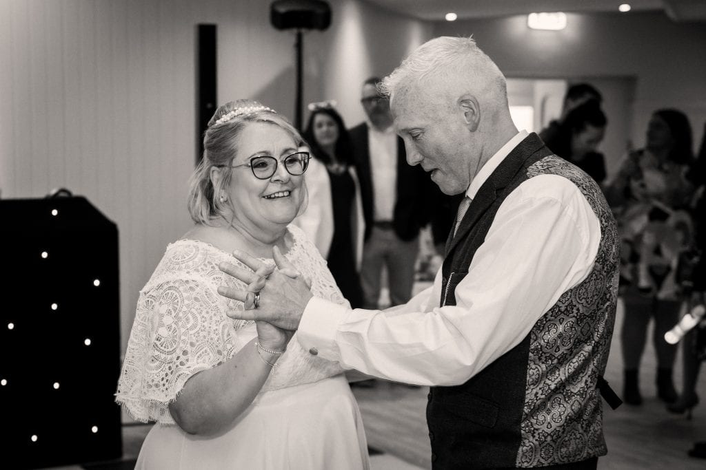 A couple dances together at a wedding reception, surrounded by guests.