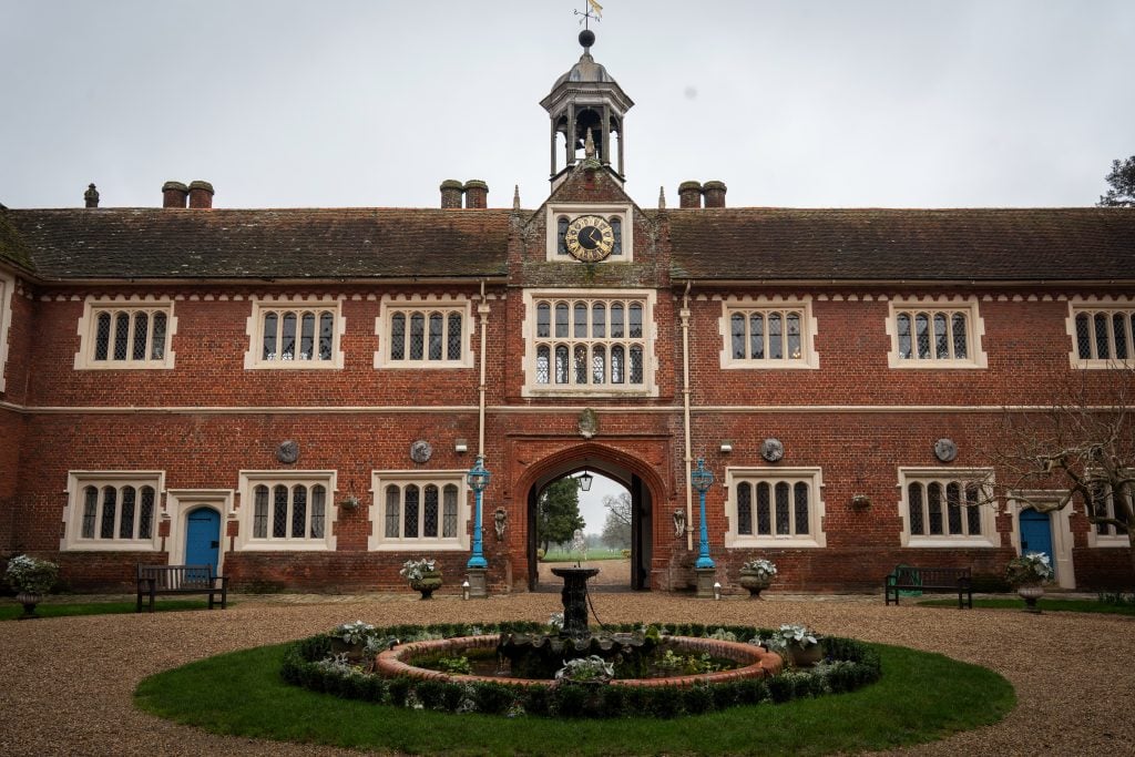 A historic red-brick building with a clock tower, arched entrance, and symmetrical windows, set behind a circular fountain and gravel courtyard. Wedding Photo taken by Jennings Photography