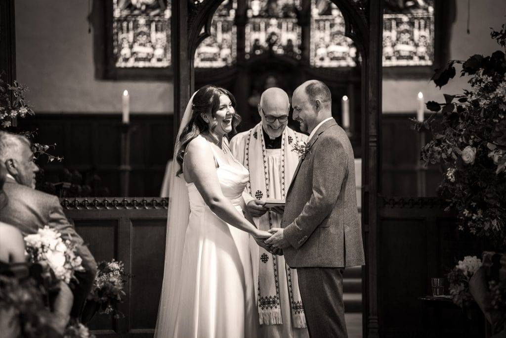 A bride and groom stand holding hands and smiling at each other during their wedding ceremony in a church, with an officiant present. Wedding Photo taken by Jennings Photography